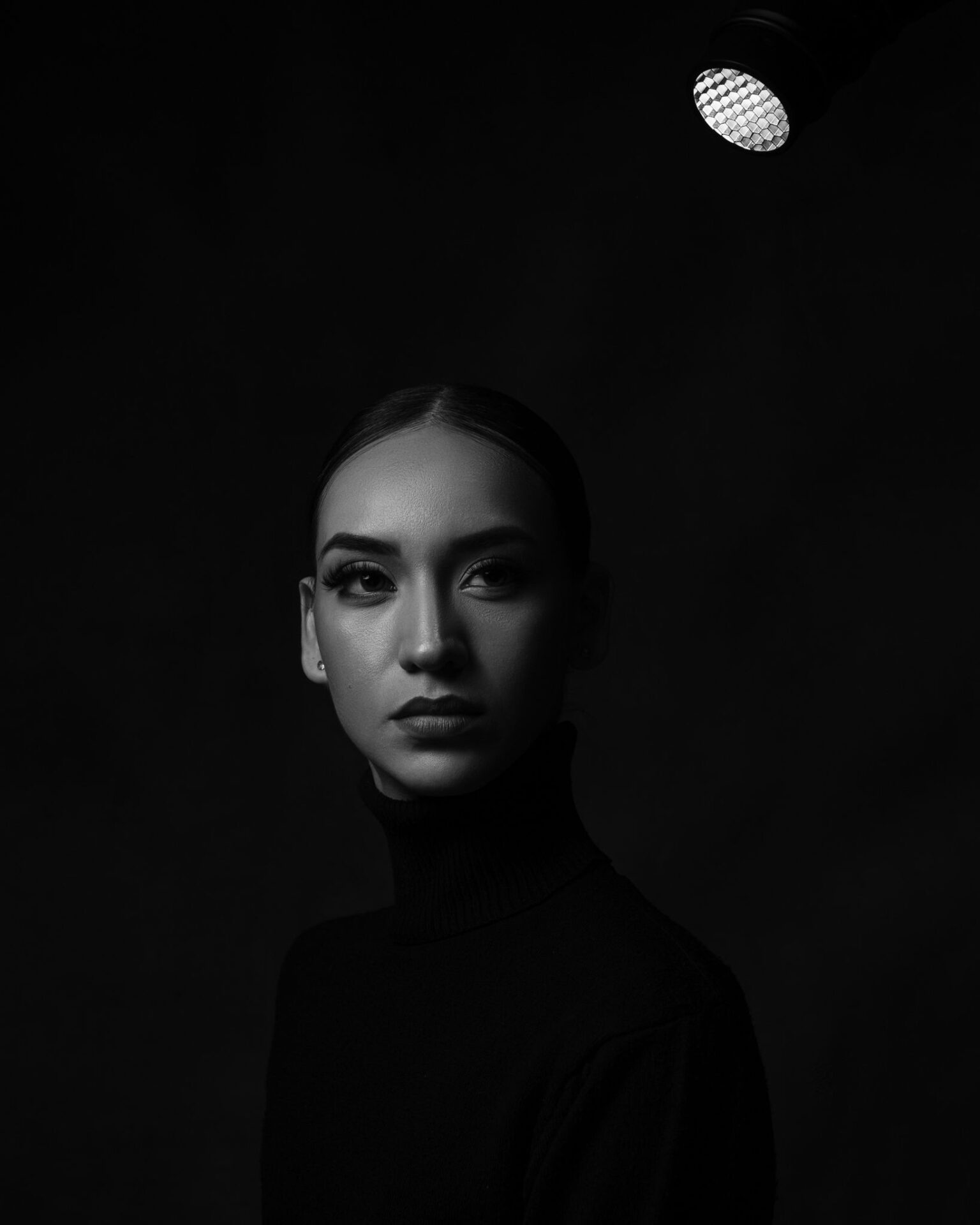 Elegant black and white portrait of a woman under spotlight, moody and dramatic.