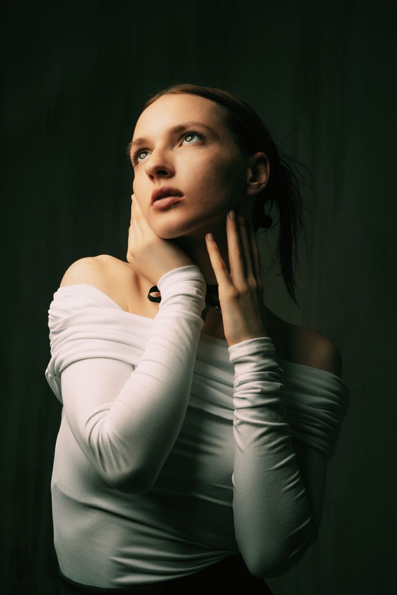 Moody portrait of a woman in a white blouse with hands on her neck in fashion style.